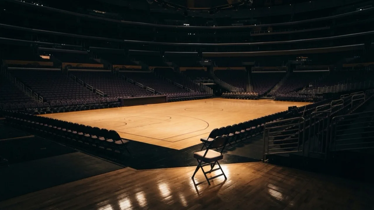 Empty basketball arena at night with courtside seats lit by overhead lights